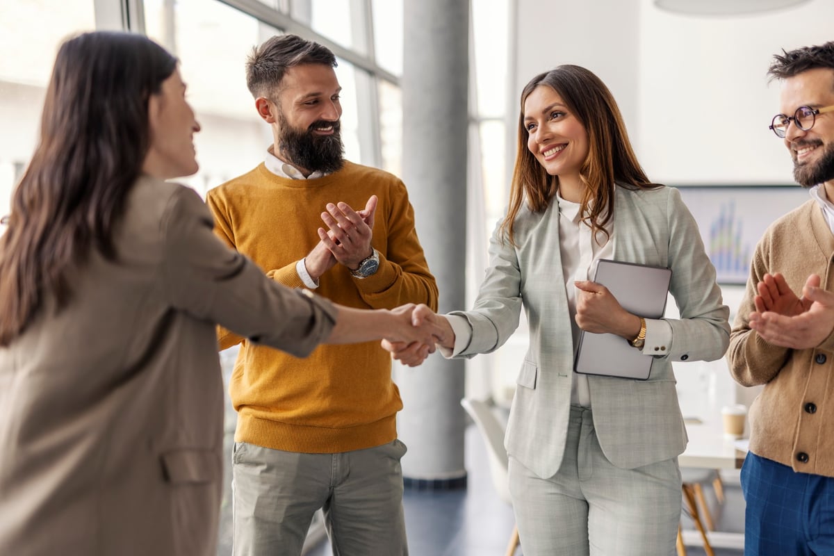 Two successful female executives shaking hands for partnership and standing at office