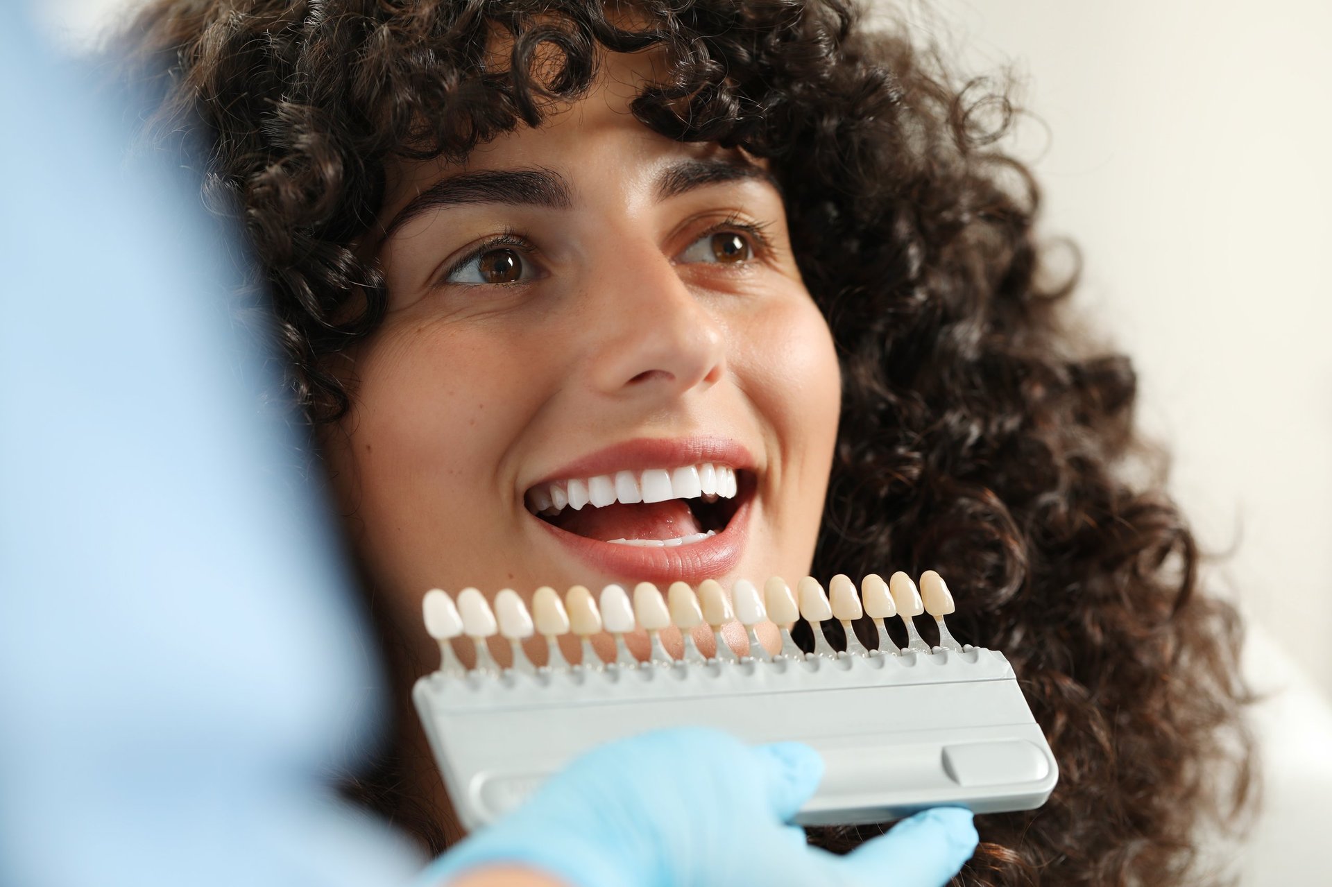 Dentist checking a young woman's tooth shade in a clinic, cosmetic dentistry veneers closeup