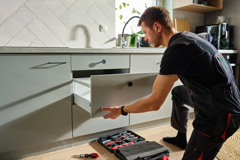 Man assembling kitchen drawer in modern cabinet using screwdriver during furniture installation