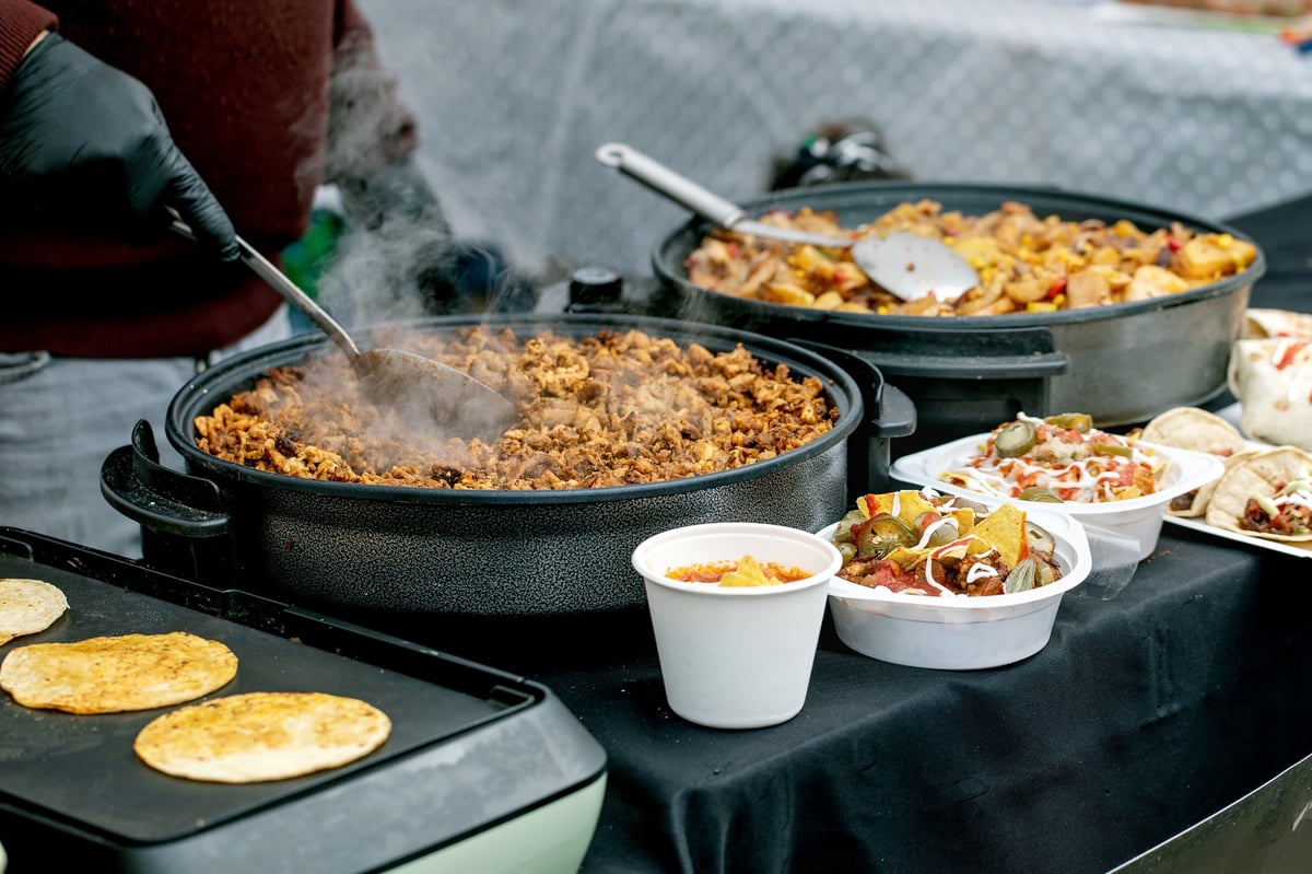 Mexican street food preparation with cook stirring meat in cast iron pan at outdoor market