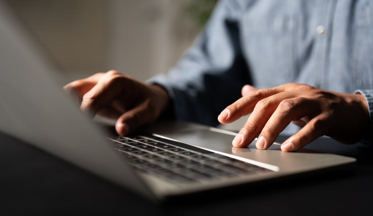 A man using and typing keyboard of laptop computer communicates on internet technology with paperwork on office desk