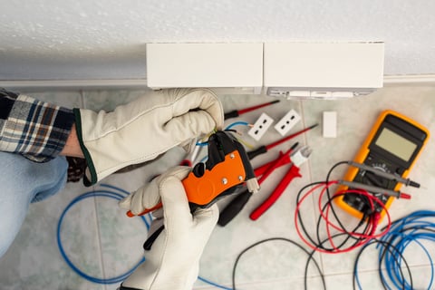Electrician using wire stripper pliers to prepare electrical cables at a residential panel