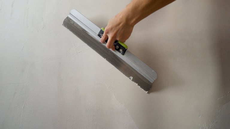 Construction worker smoothing wet plaster on wall using a spatula during renovation work