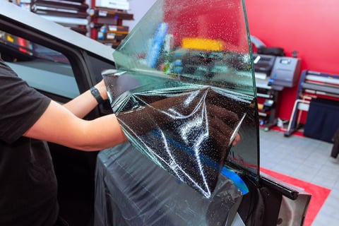 Worker applying tinted film to car window
