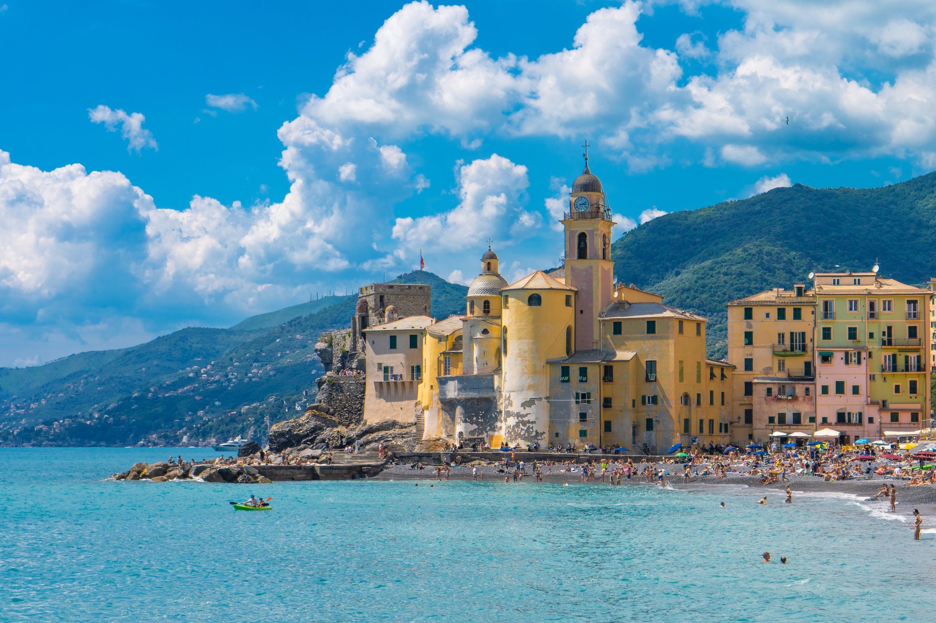 Wide view of the Mediterranean seaside village of Camogli, Italy, with colorful buildings along turquoise water under a bright blue sky