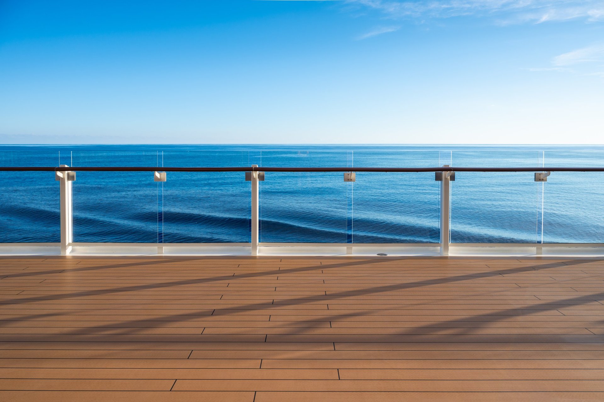 Elegant wooden cruise ship deck with glass railings looking out over calm blue sea and sky