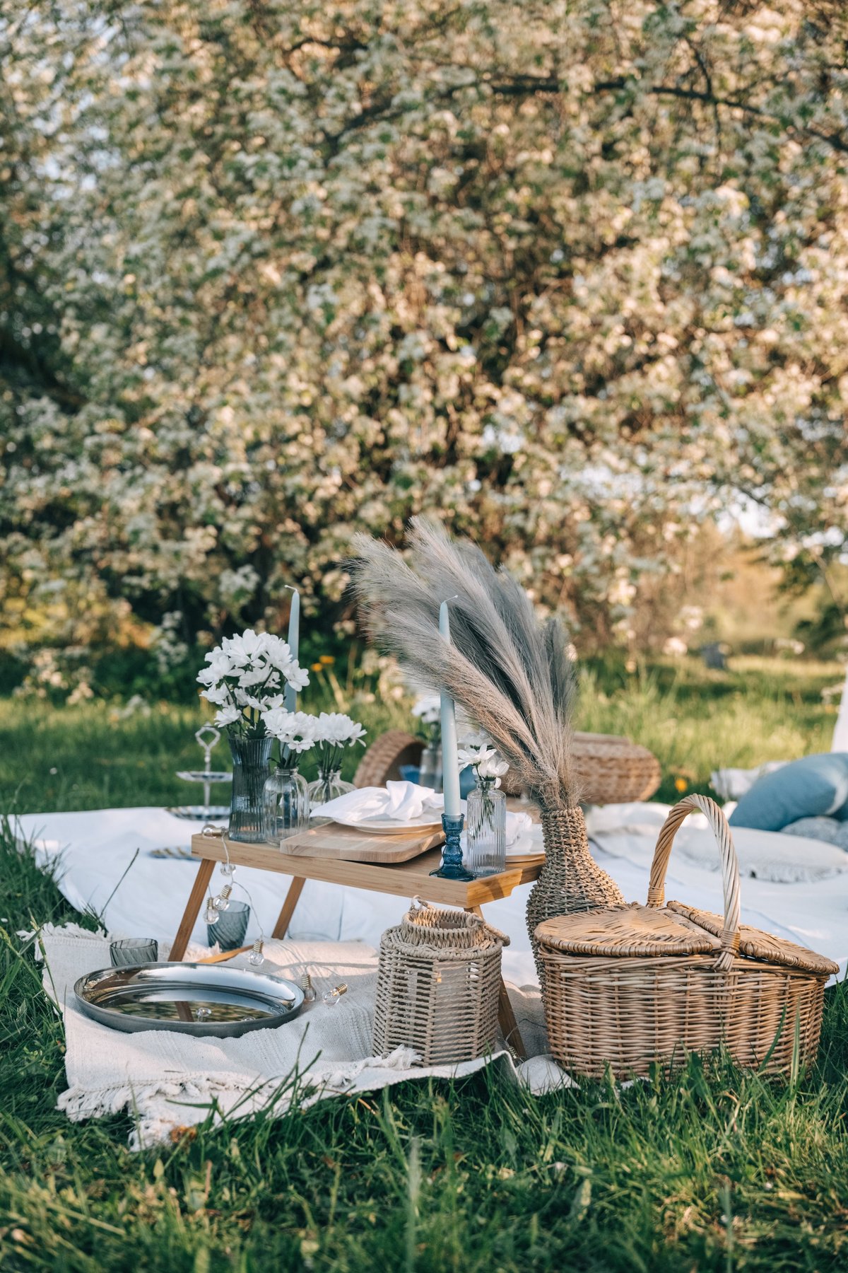 An inviting luxury picnic arrangement with woven baskets, floral centerpieces, and pastel styling in a meadow setting