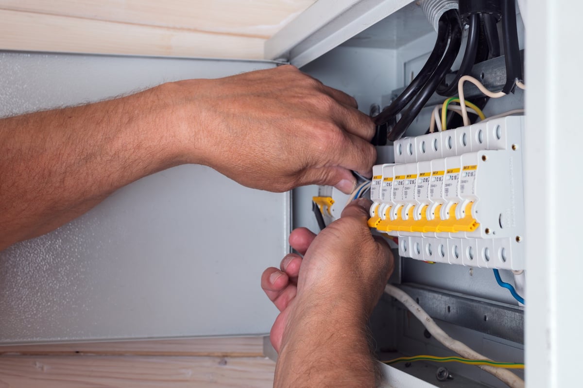 Elektriker verbindet Kabel in einem offenen Verteilerschrank – fachgerechte Verbindungen für sichere Stromnutzung