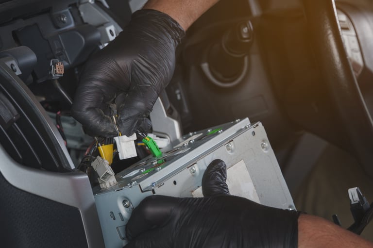 Close-up of an automotive technician's hands while unplugging electrical connectors from a car stereo unit during disassembly