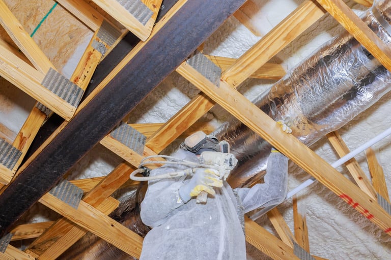 Construction worker installing thermal barrier insulation in attic with spray equipment