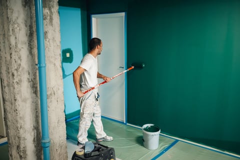 Professional painter applying paint with roller on interior wall