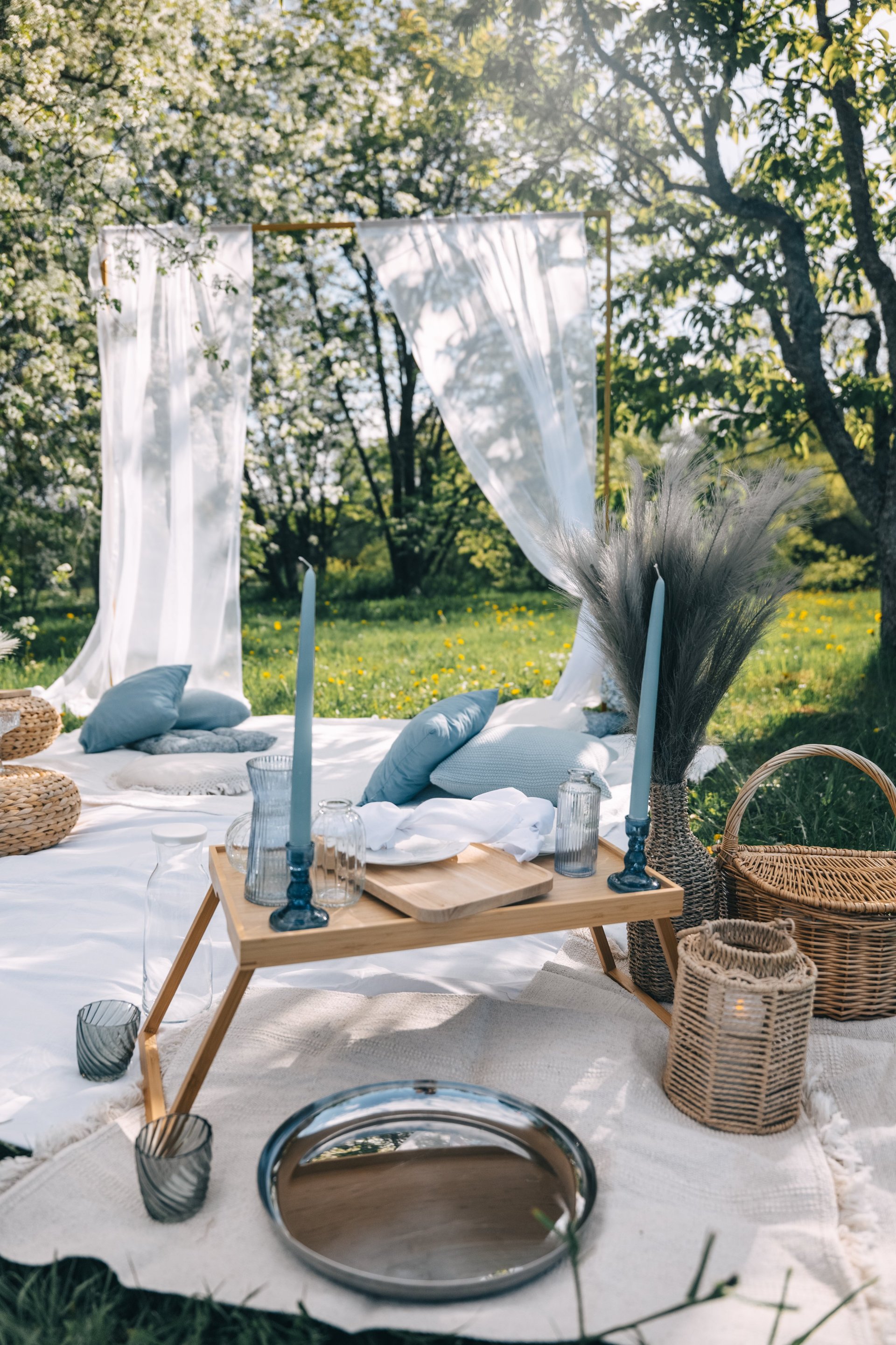 A charming outdoor luxury picnic arranged with cushions, candles, and pastel decor in a sunlit grassy meadow