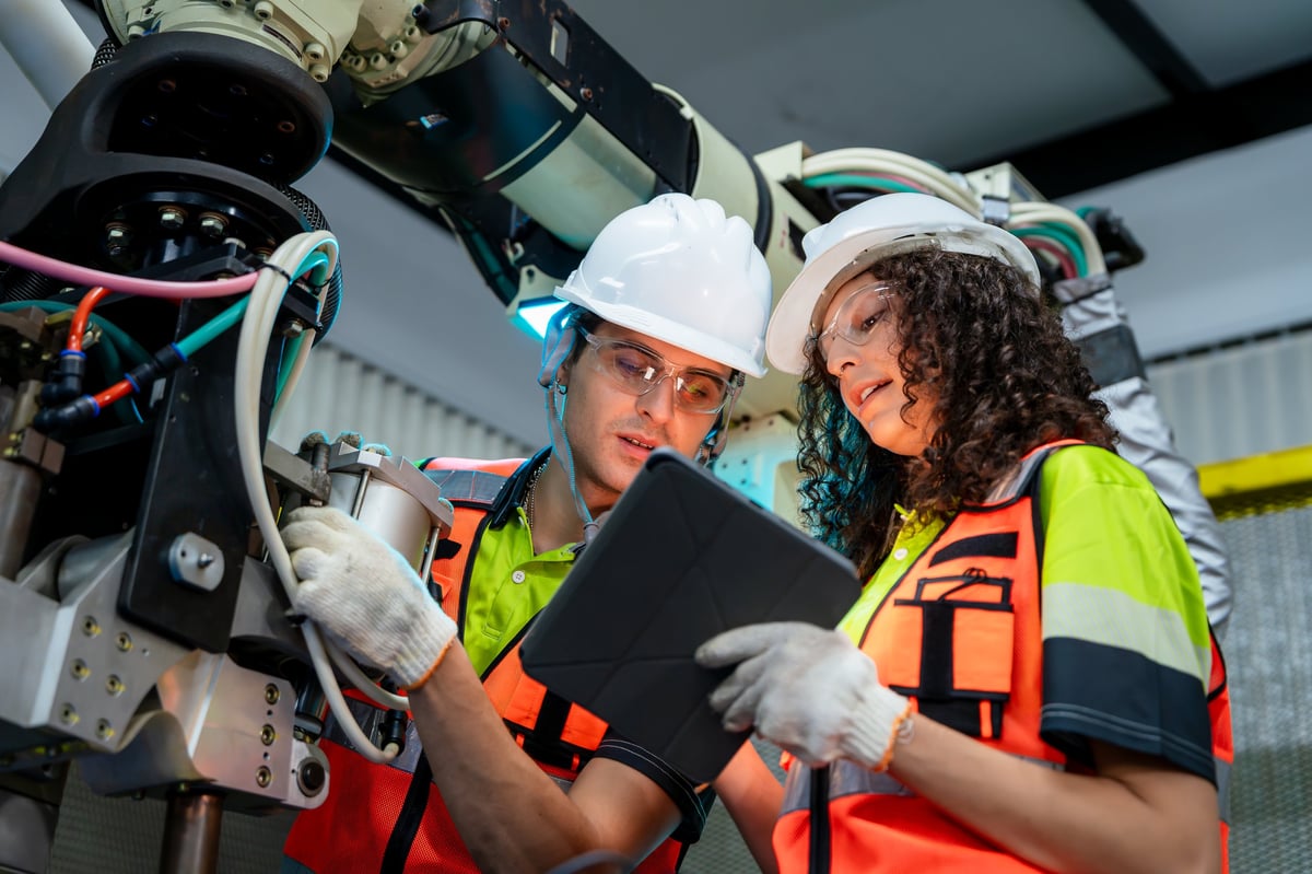 Two people wearing safety gear and holding a tablet, with diverse engineers collaborating on automation technology