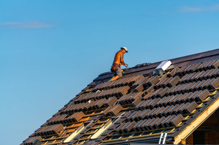 Roofer working on a house installing metal roofing, viewed from behind