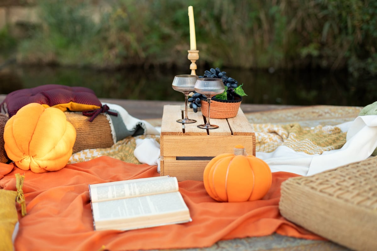 Cozy boho autumn picnic on a pier with carpet, cushions, plaid blanket, and soft styled décor