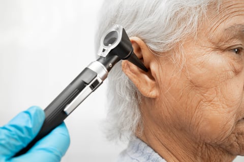 Otolaryngologist or ENT physician doctor examining senior patient ear with otoscope, hearing loss problem
