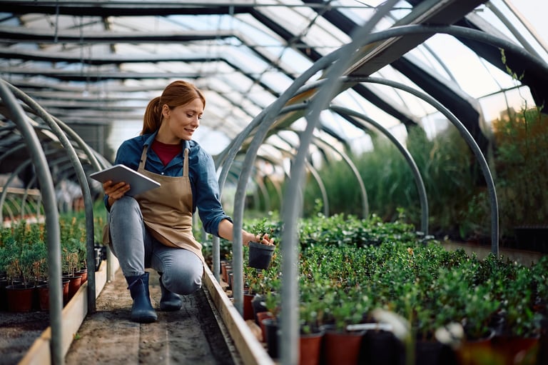 Happy female botanist using tablet while working at plant nursery
