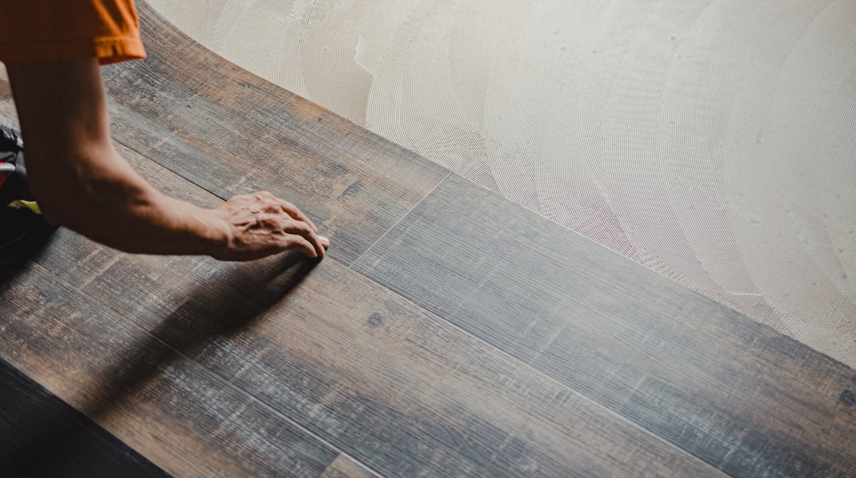 Professional builder laying vinyl tile flooring with adhesive