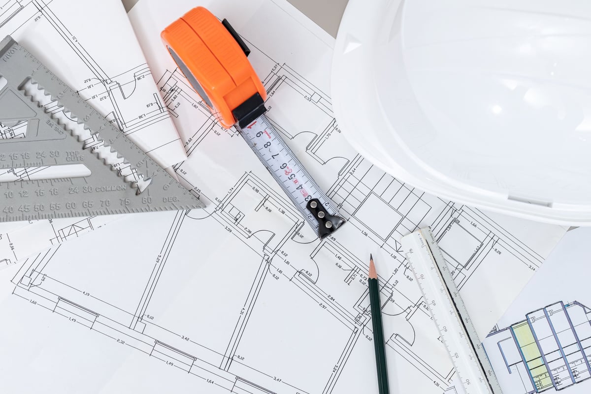 Plano de obra sobre una mesa de trabajo con cinta métrica, casco y lápiz: material de consulta para las guías del blog