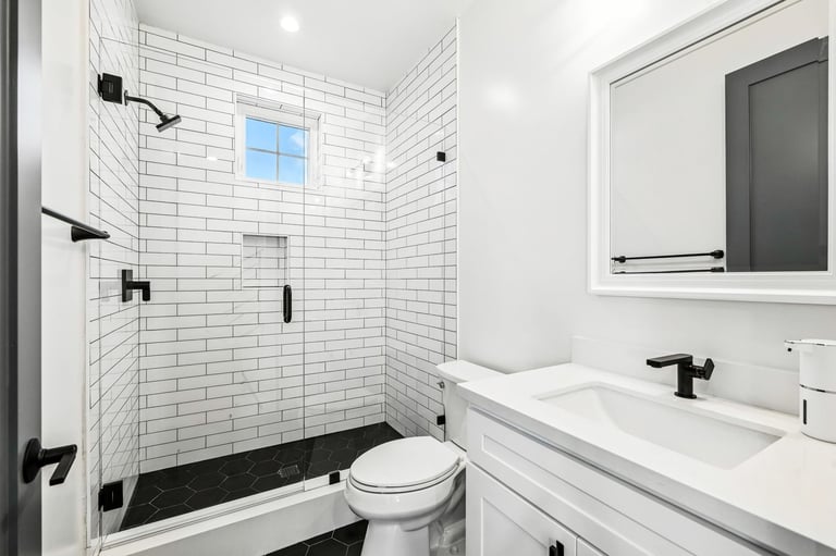 Modern white bathroom with subway tiles, black fixtures, and a glass shower door