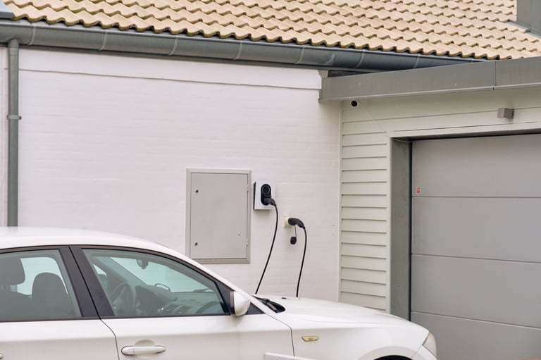 White electric car with wall charger plugged in at home driveway