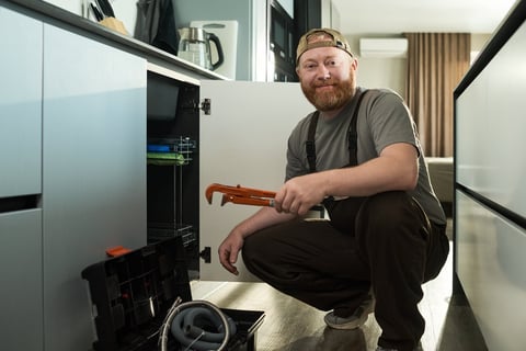 Handyman kneeling in kitchen holding pipe wrench performing repair work