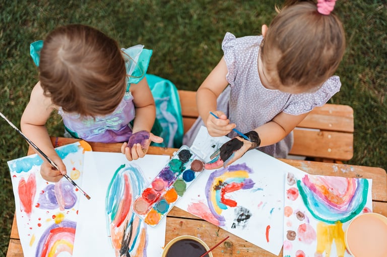 Two preschool-age girls painting rainbows outdoors