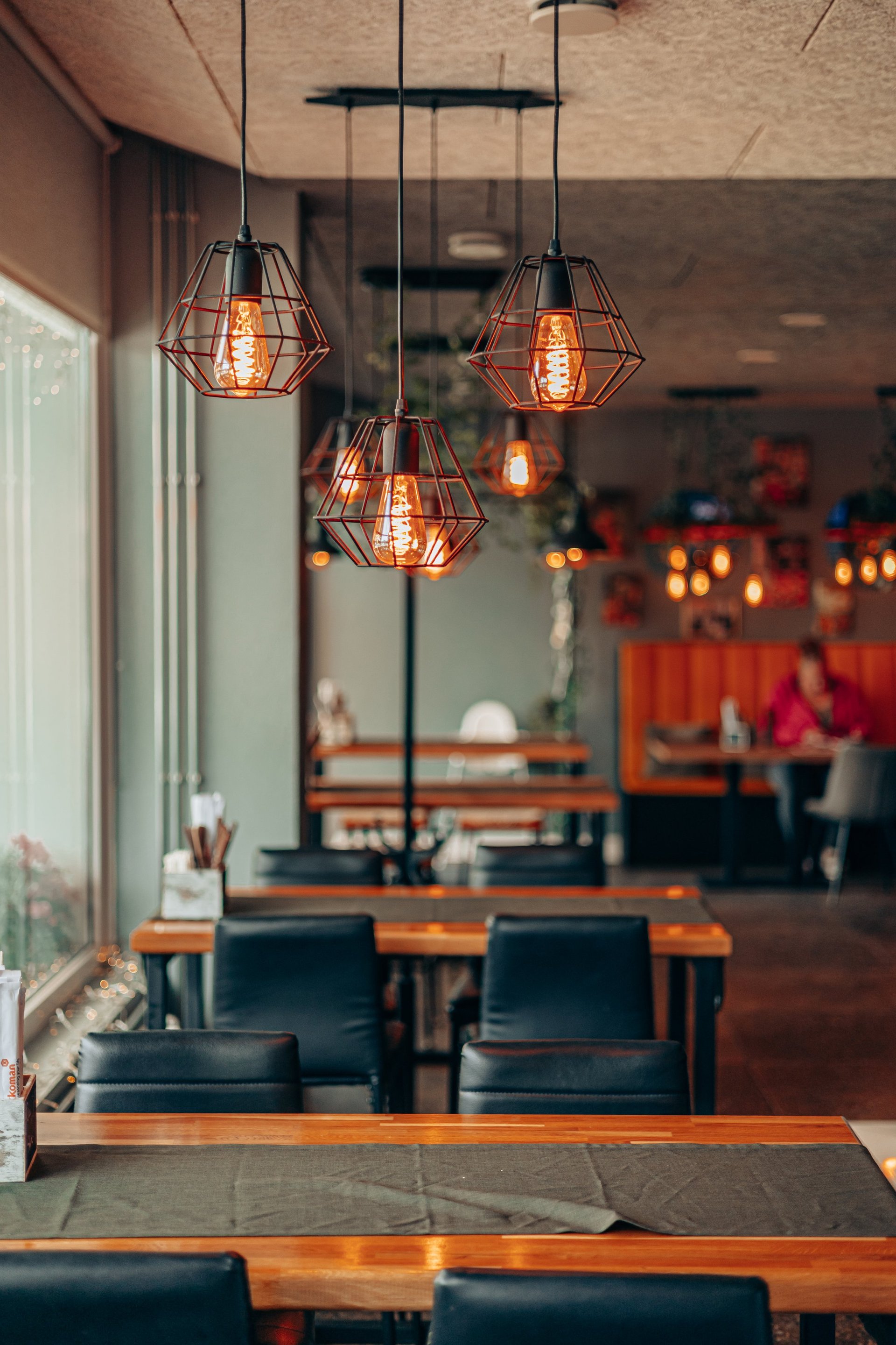 A warm, modern restaurant interior with Edison bulb lighting, wooden tables and black chairs