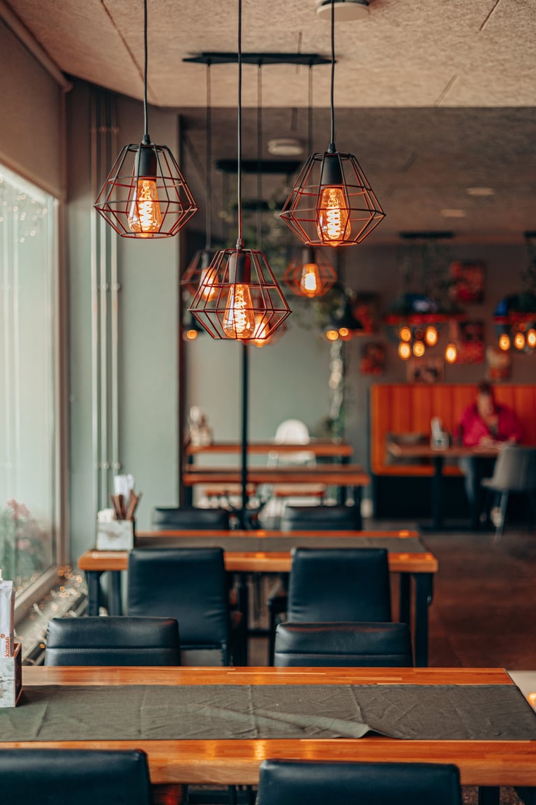 Warm cafe interior with Edison bulb lighting, wooden tables and black chairs