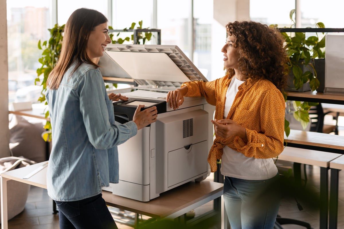 Two businesswomen collaborating at a multifunctional printer in a modern office