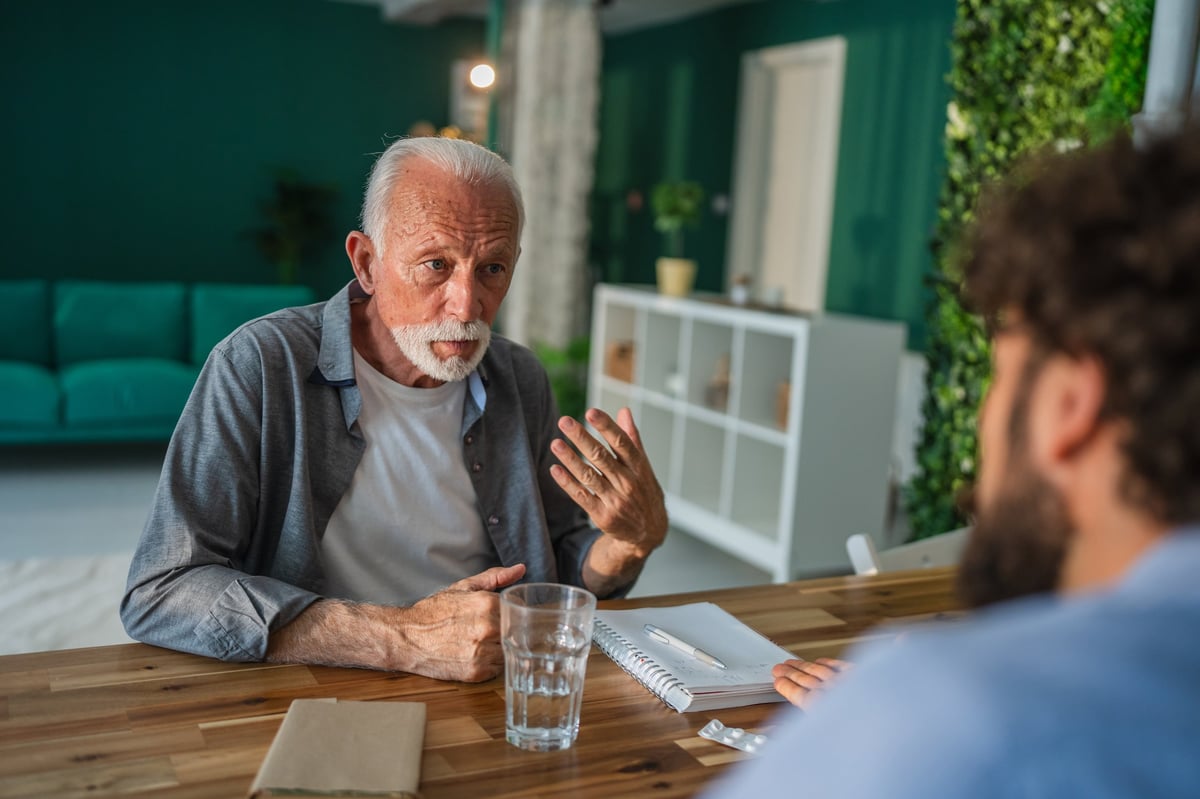 Healthcare coordinator discussing elderly parent care with senior man during home visit — chronic care management and family communication