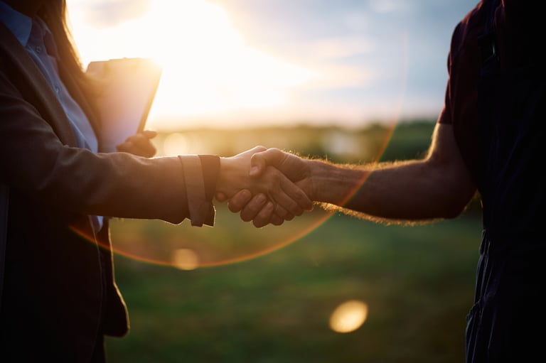 Businesswoman and farm owner shaking hands in the field at sunset