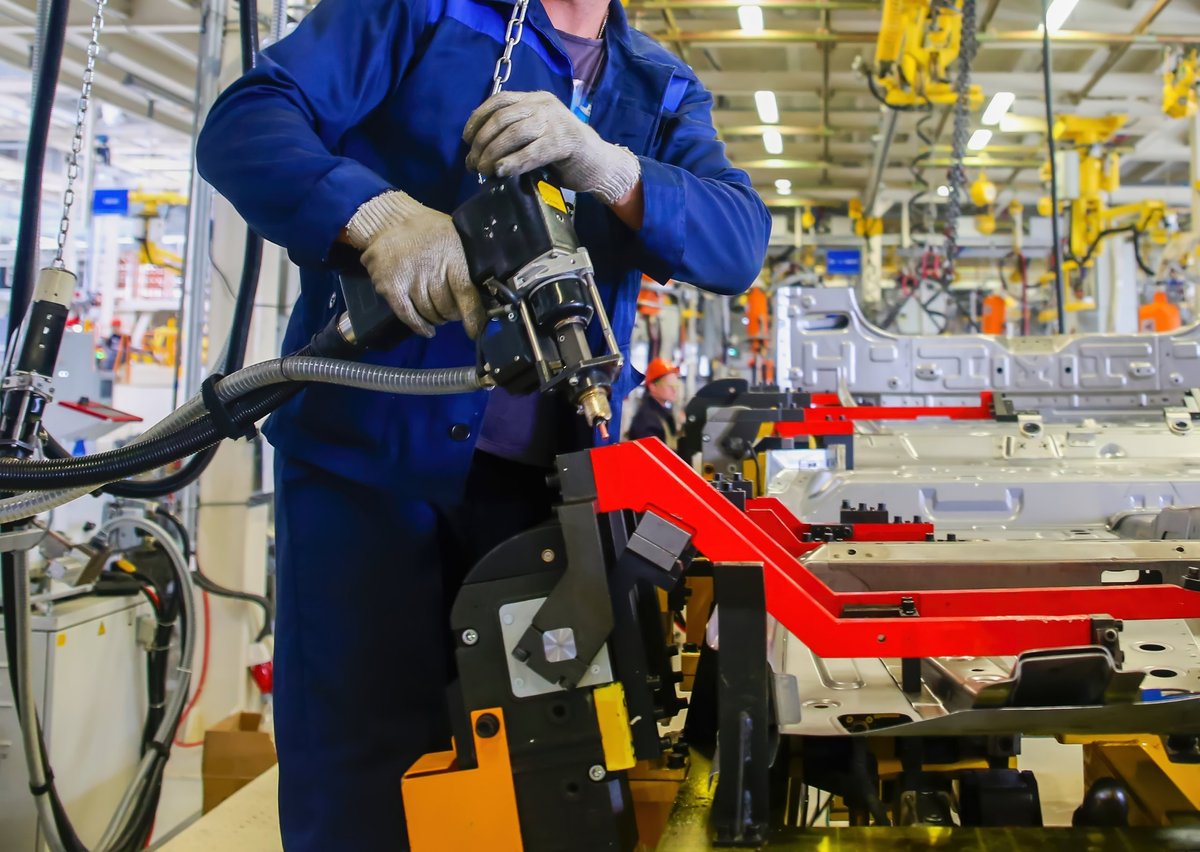 Skilled technicians work on automotive parts using advanced tools and machinery in a busy production hall filled with equipment