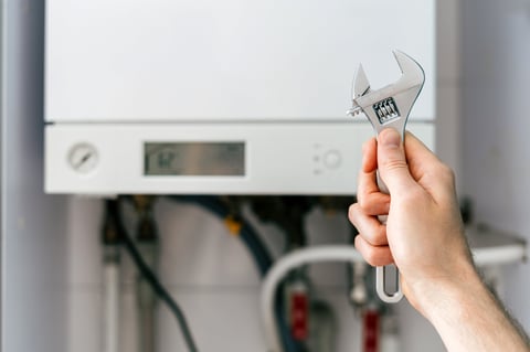 Water heater repair technician adjusting boiler with wrench in utility room