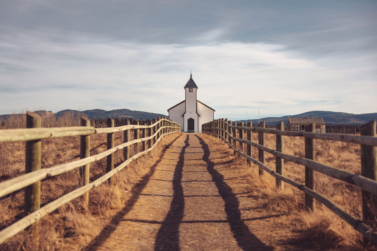 Historic rural church at the end of a wooden fence pathway under open sky