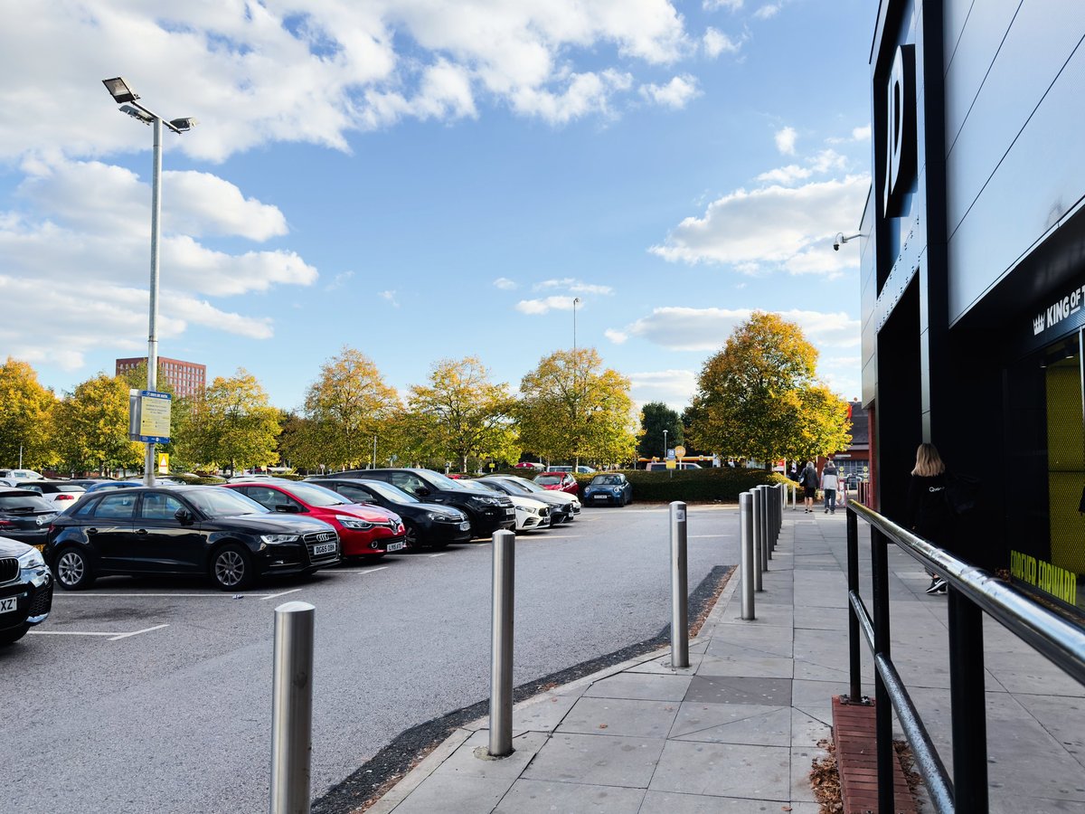 Modern parking lot with cars parked in front of a glass storefront under a blue sky