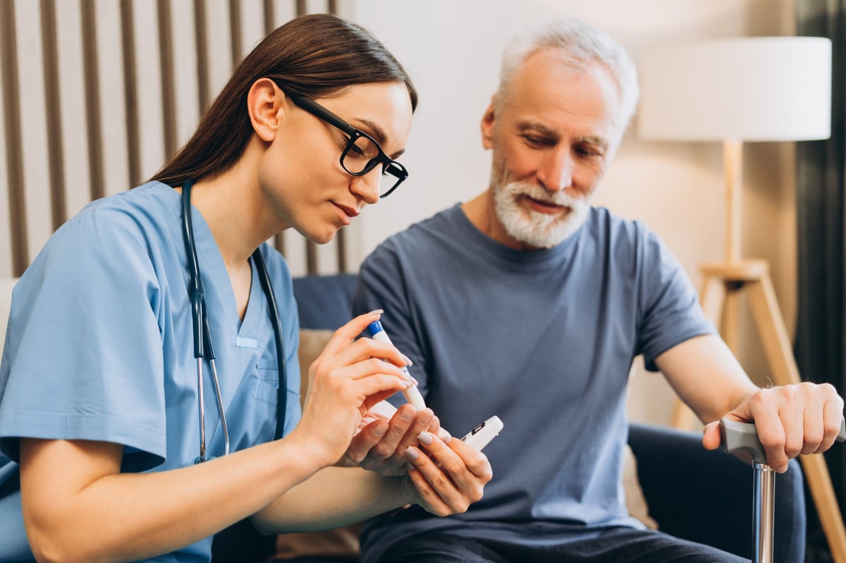 Nurse assisting senior man with glucometer to check blood sugar for diabetes