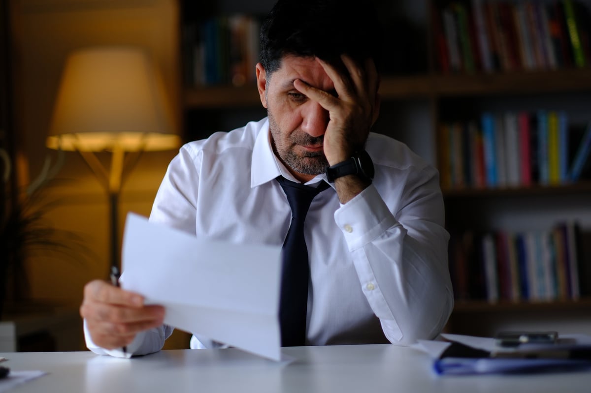 Businessman looking concerned while reviewing paperwork and bills at his desk