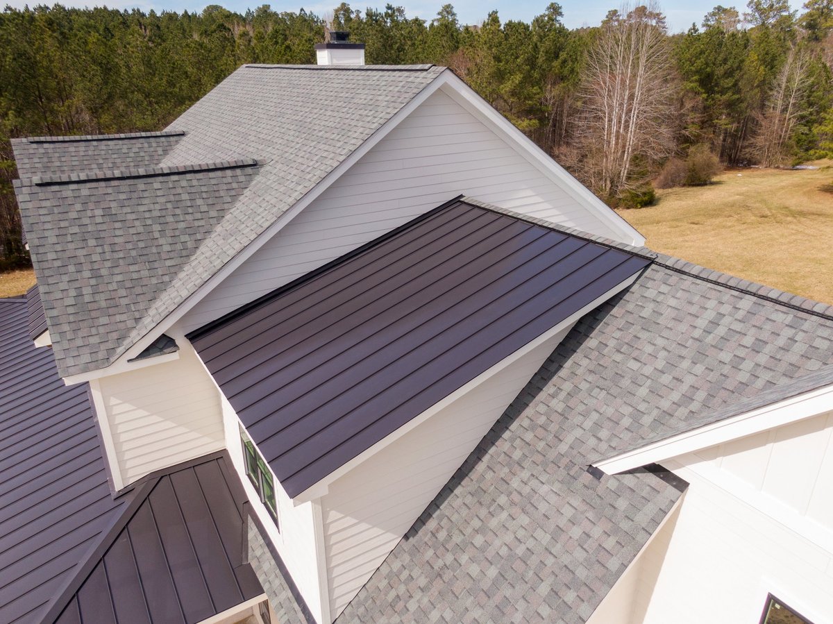 Drone aerial image of a custom residential home featuring a combination of asphalt shingles and standing seam metal roofing