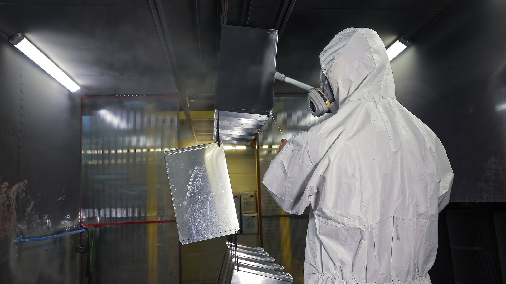 Operador con traje de protección aplicando pintura en polvo a componentes metálicos