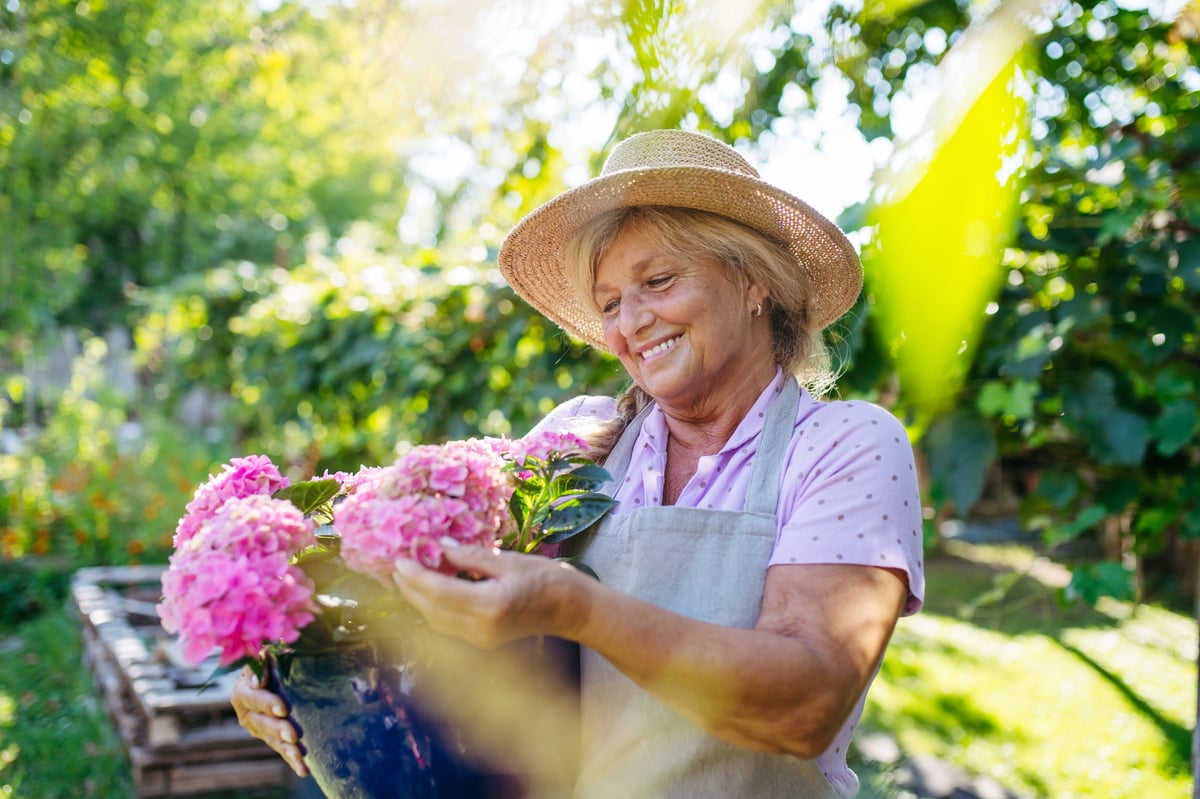 Señora mayor sonriendo mientras cuida plantas y flores en el jardín