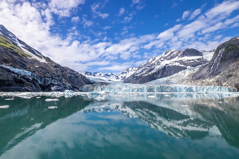 Massive tidewater glacier with snow-covered peaks reflected in an Alaskan fjord