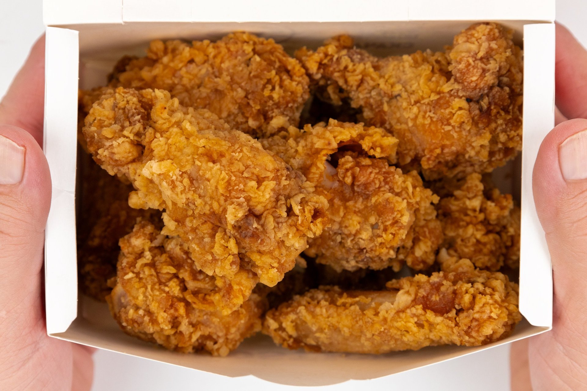 Hands holding a takeout box filled with golden crispy Krispy Krunchy Chicken