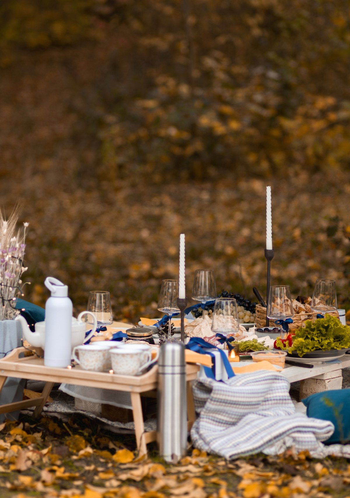 Cozy picnic setup with candles, fairy lights, pillows, blankets, and soft autumn styling