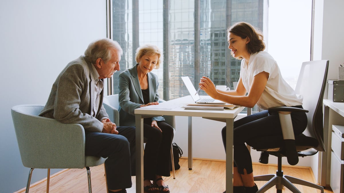 Senior couple receiving Medicare & Medicaid navigation and geriatric care management from a female financial advisor in a professional office