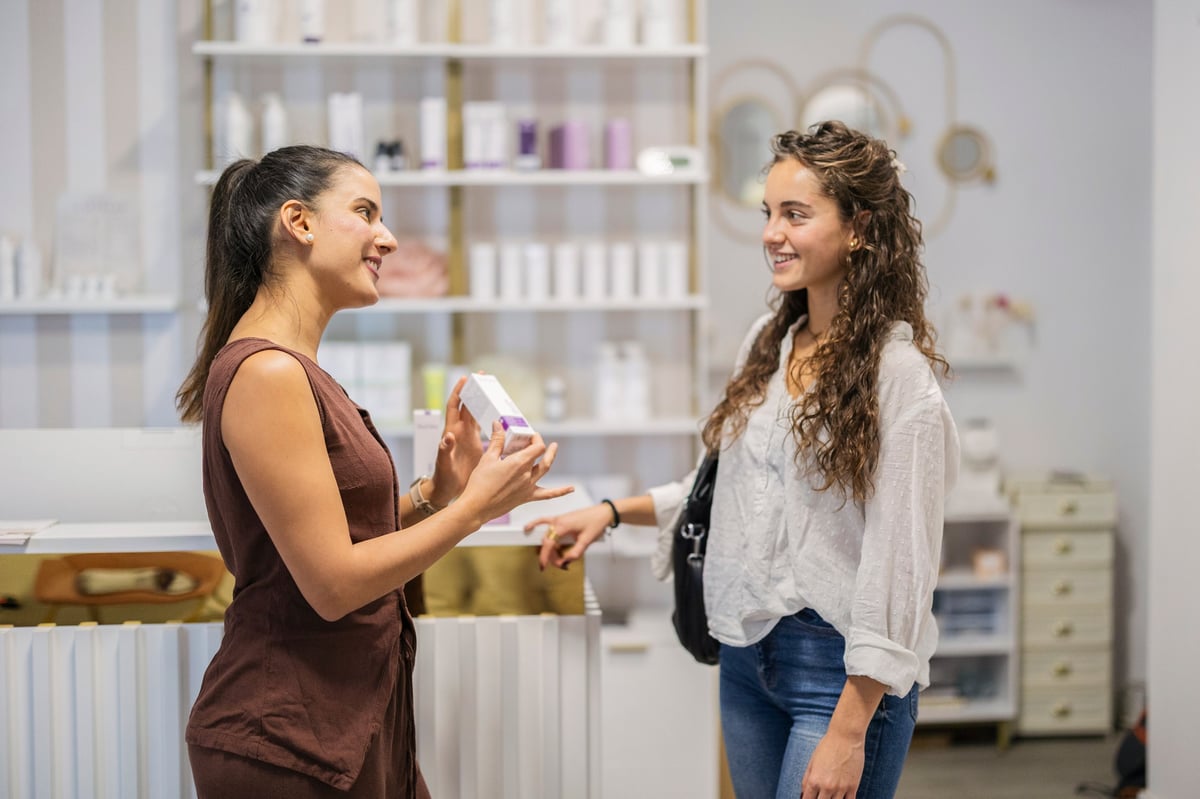 Professional beauty consultant presenting a skincare product to a smiling customer