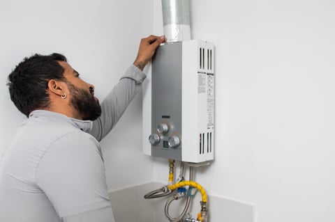 Technician inspecting tankless water heater venting pipe for maintenance service