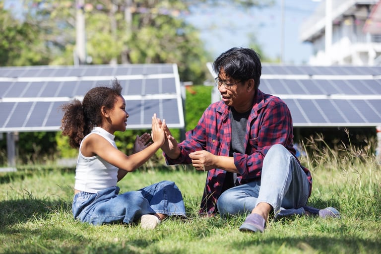 Father and daughter sharing a joyful high five while learning about clean energy near solar panels
