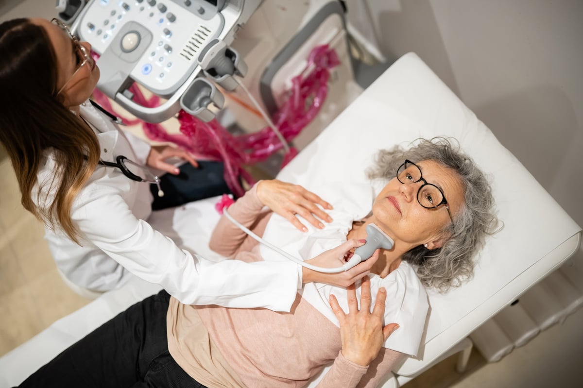 Doctor performing thyroid ultrasound exam on senior female patient