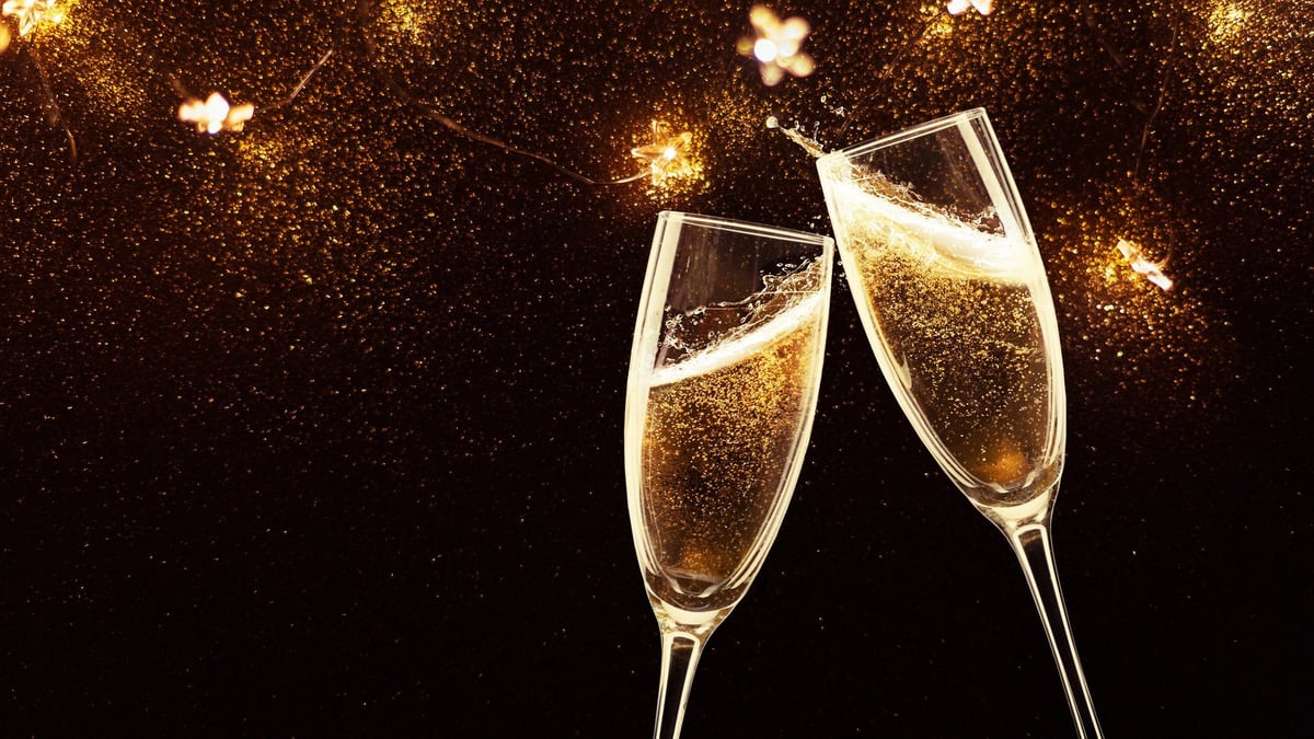 Two champagne flutes clinking with prosecco against golden bokeh backdrop
